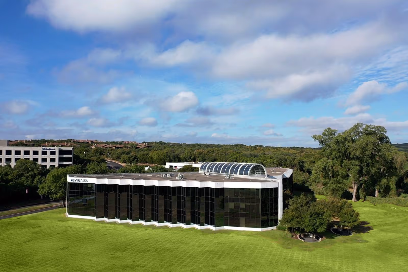 Exterior view of a modern glass building on a grassy landscape beneath a blue sky