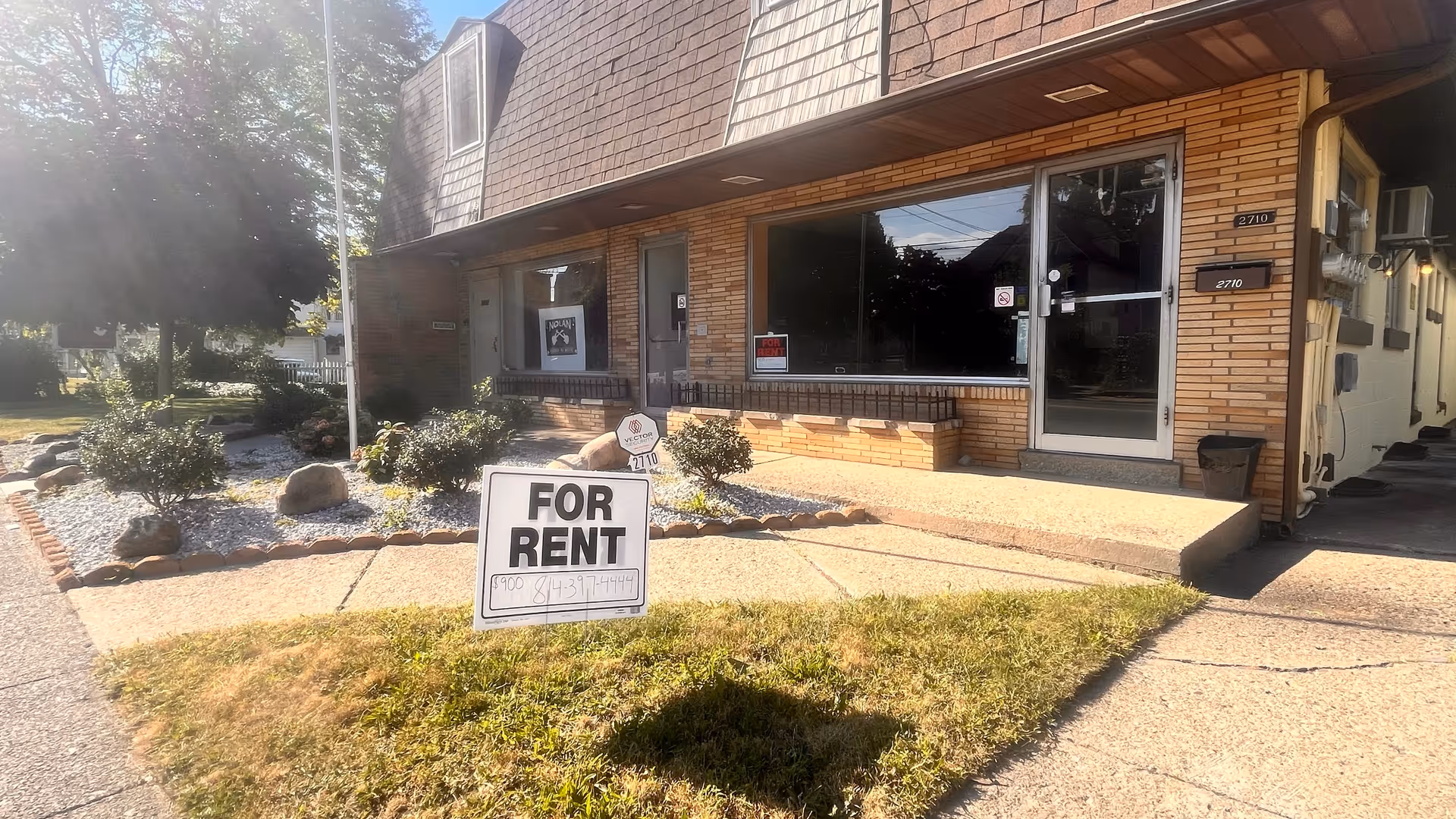 Brick building exterior with large front windows and a prominent 'FOR RENT' sign.