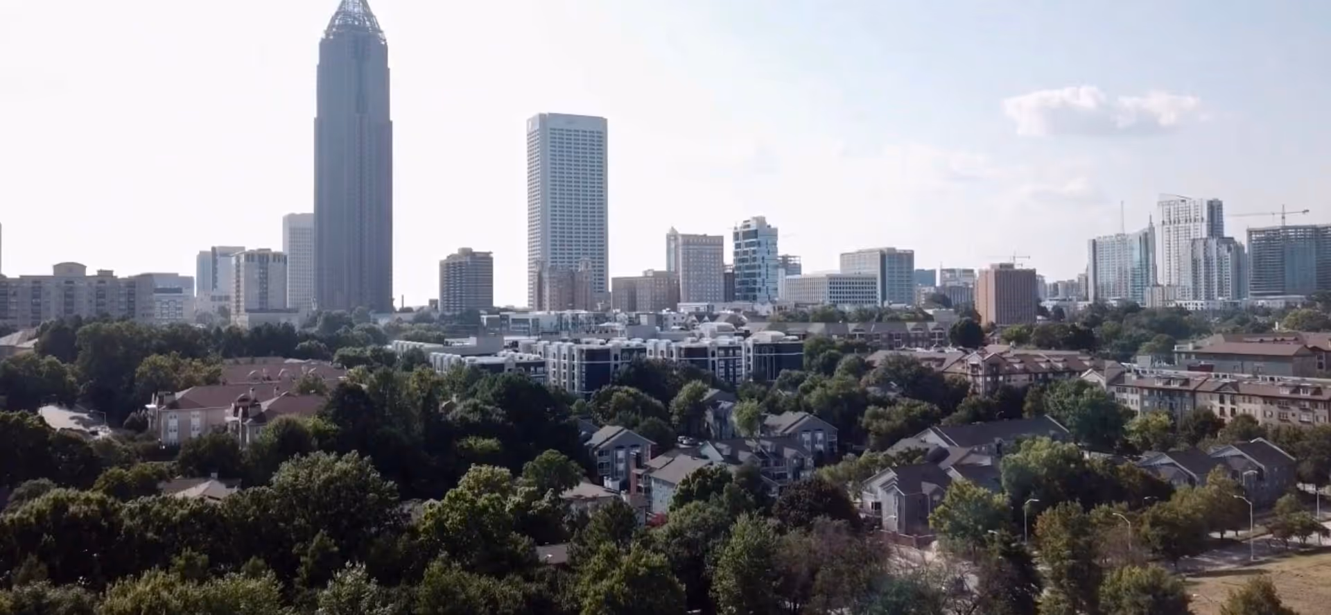 A city skyline with tall buildings overlooking a residential neighborhood and tree-lined streets.