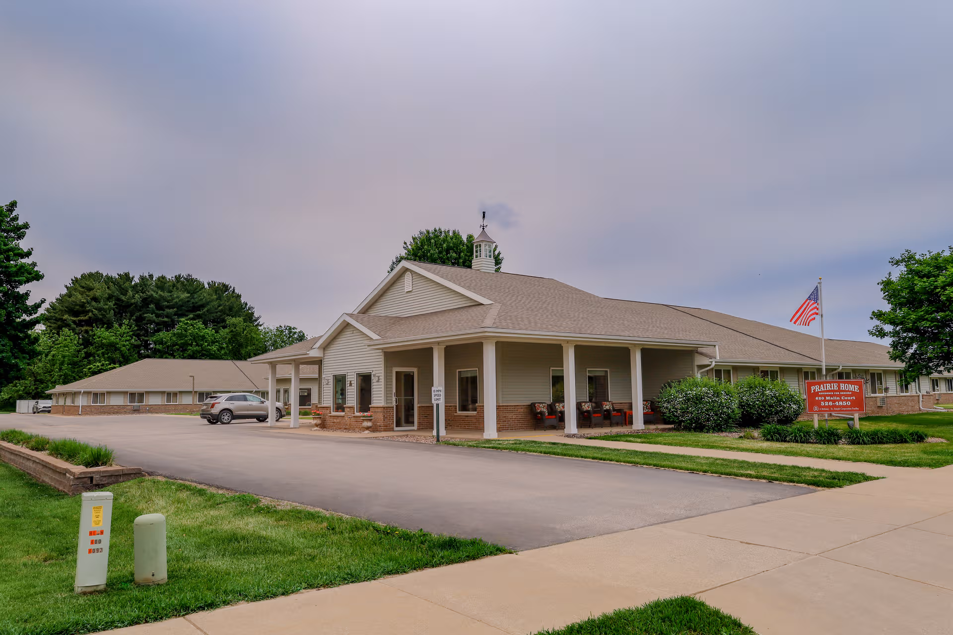Exterior of Prairie Home senior living facility with entrance, flag, and surrounding lawn.