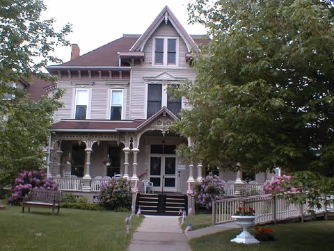 A large Victorian-style senior living facility with a front porch and landscaped lawn.