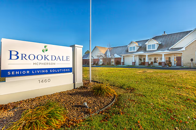 Exterior view of the Brookdale McPherson senior living facility with a large sign in the foreground and the building and lawn behind it.