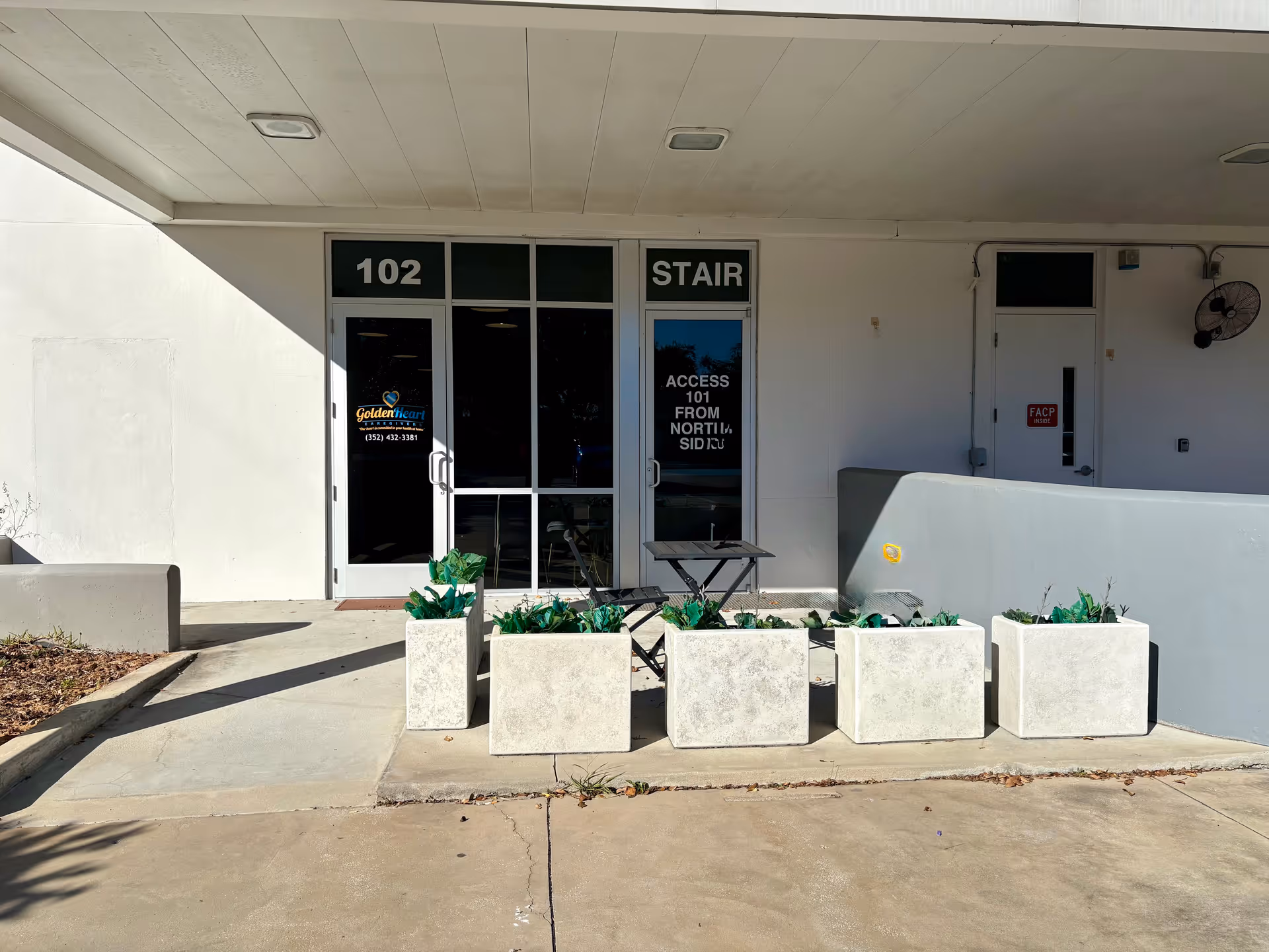 Exterior entrance to Golden Heart Caregivers facility with planters and a small seating table.
