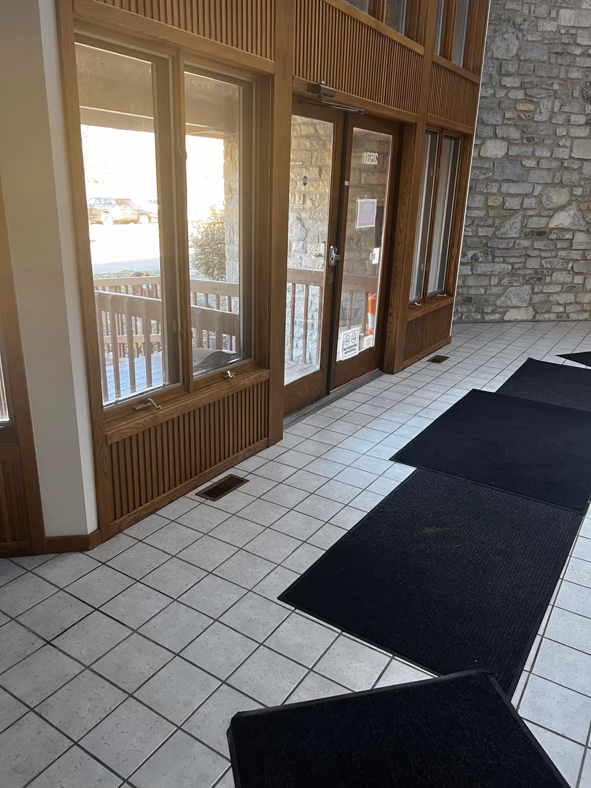 Interior entrance area with glass doors, wooden trim, tiled floor, and stone wall.