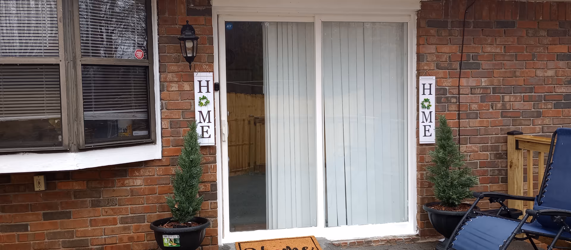 Entrance to a brick care facility with glass doors and potted evergreens.