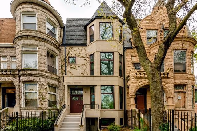 Front facade of a row of brownstone-style senior housing buildings with a large tree.