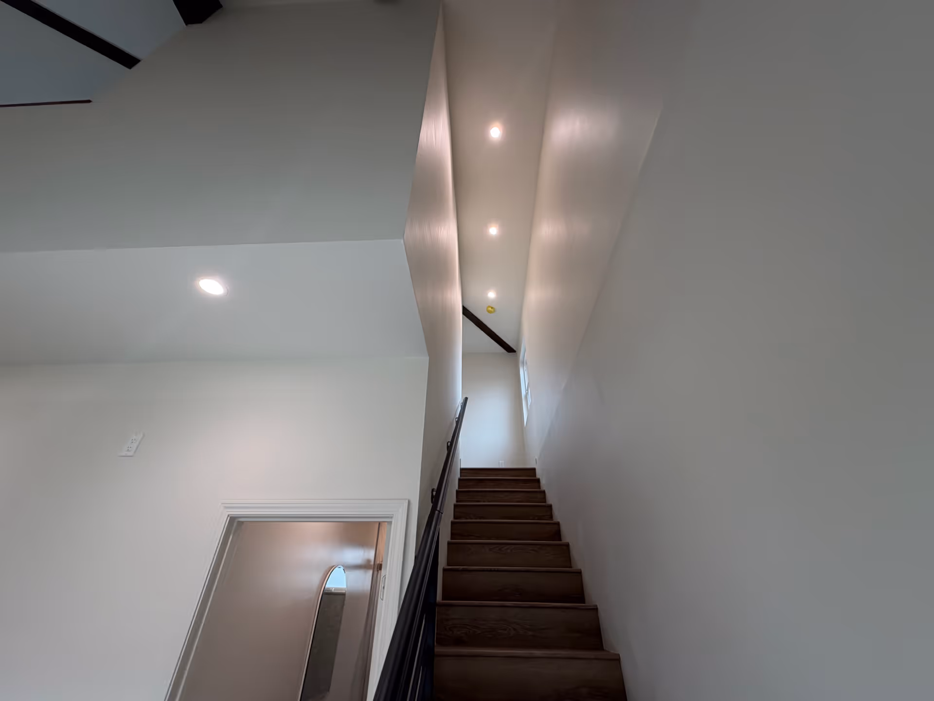 Indoor staircase with dark wooden steps, white walls, and ceiling lights.