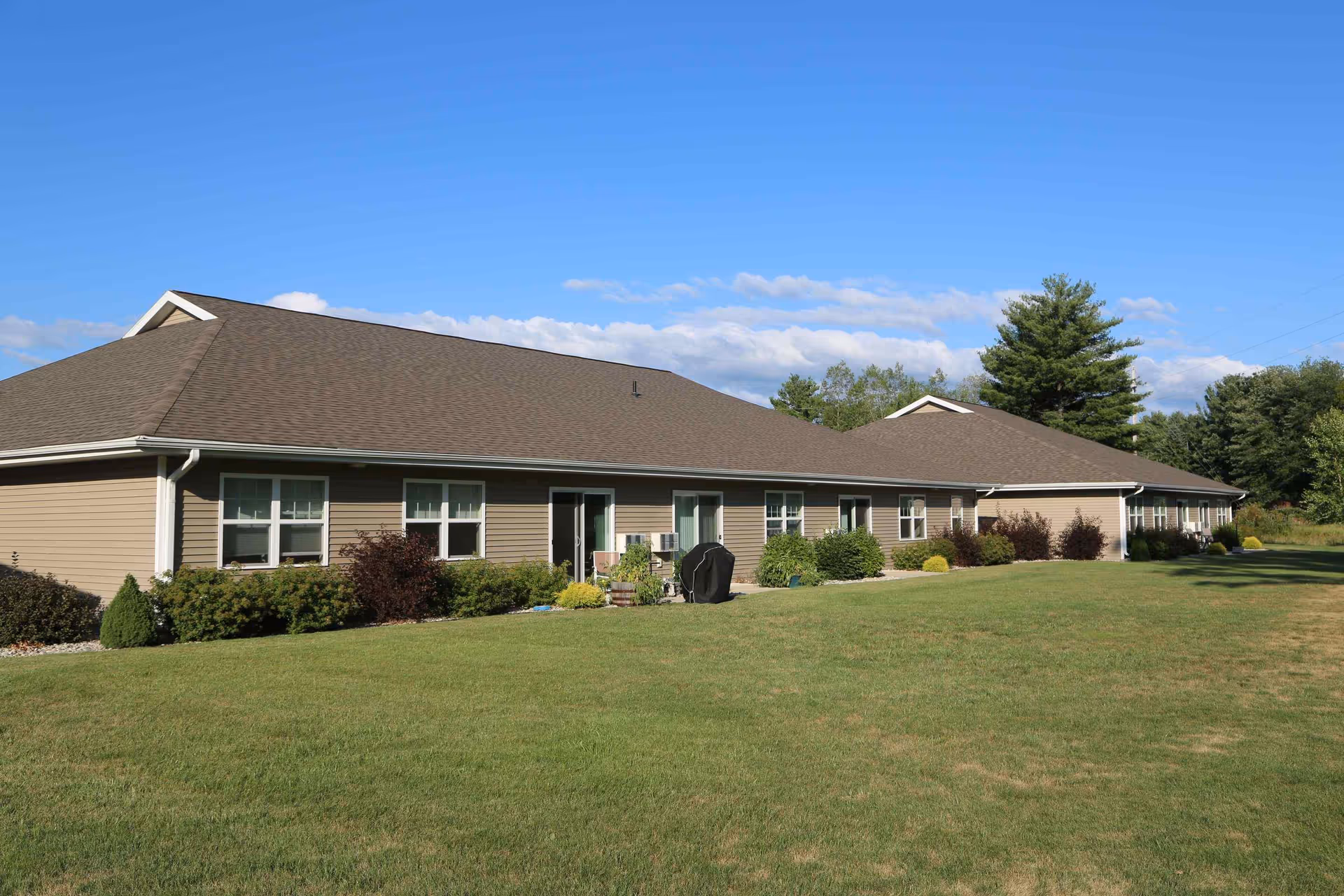 Single-story senior living facility exterior with beige siding, brown roof, and well-kept lawn.