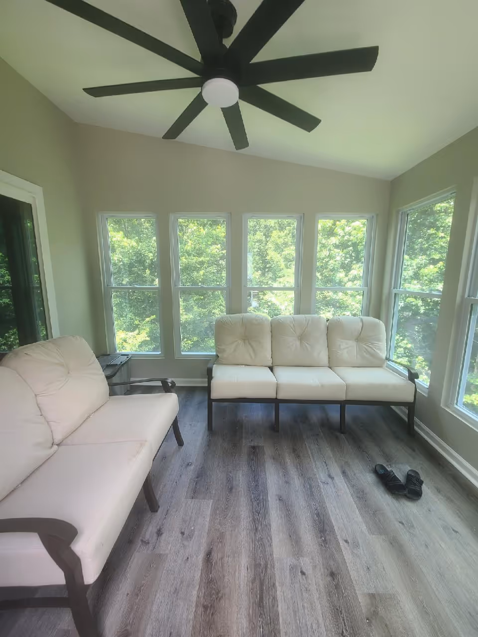 Bright sunlit living room with cream sofas, large windows, and a ceiling fan.
