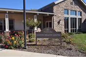 Front exterior of Westminster Village building with flower beds and a sign.