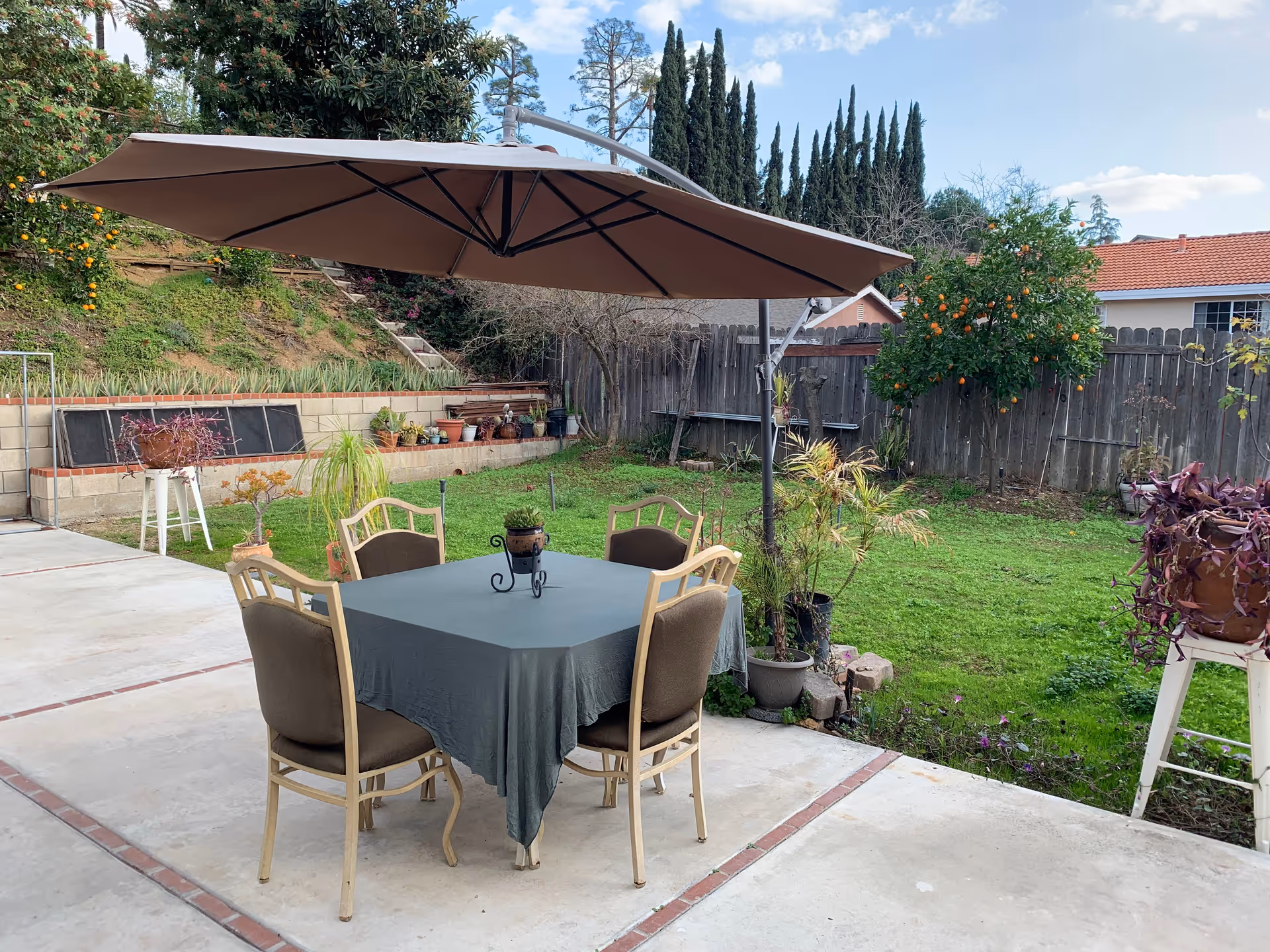 Outdoor patio with a table, four chairs, and a large umbrella in a fenced yard.