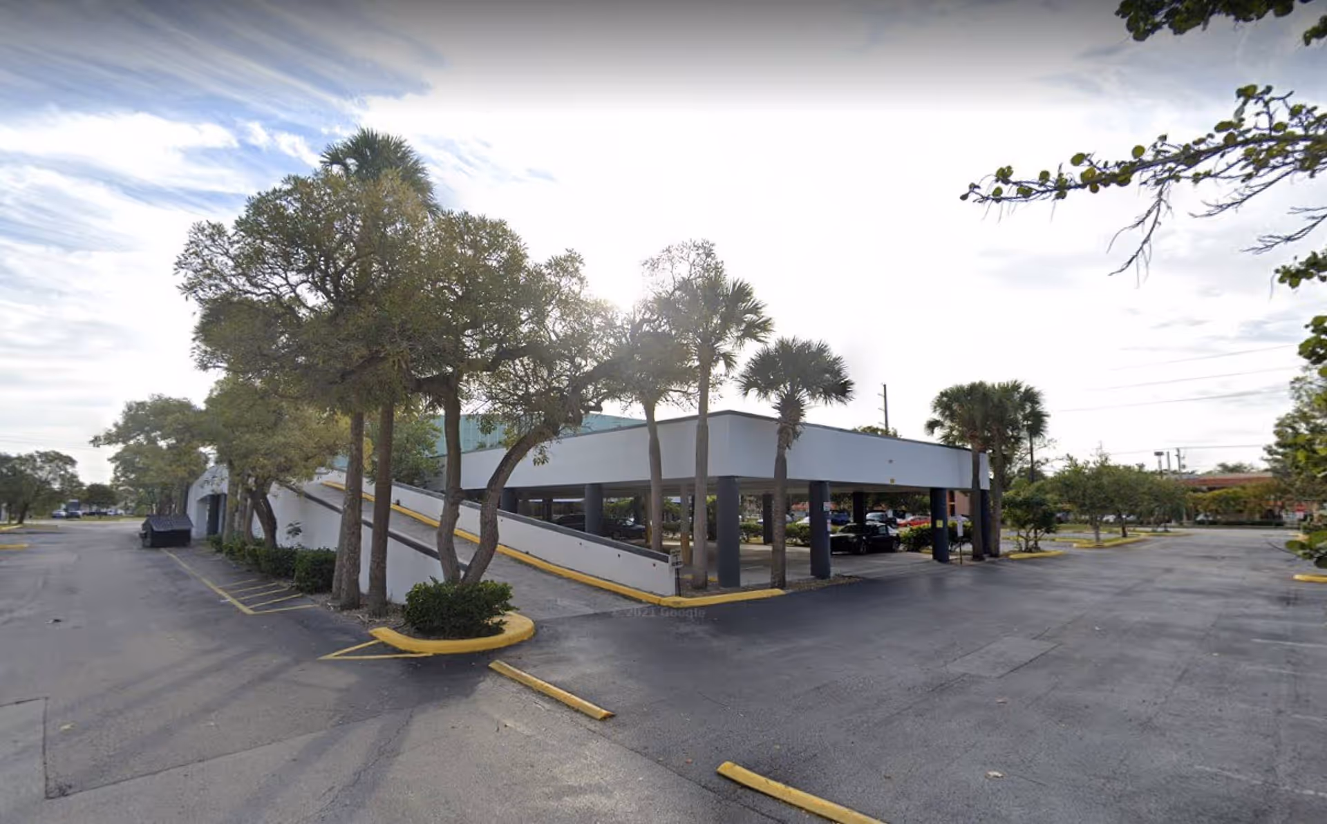 Exterior view of CareMax facility with covered parking and palm trees.