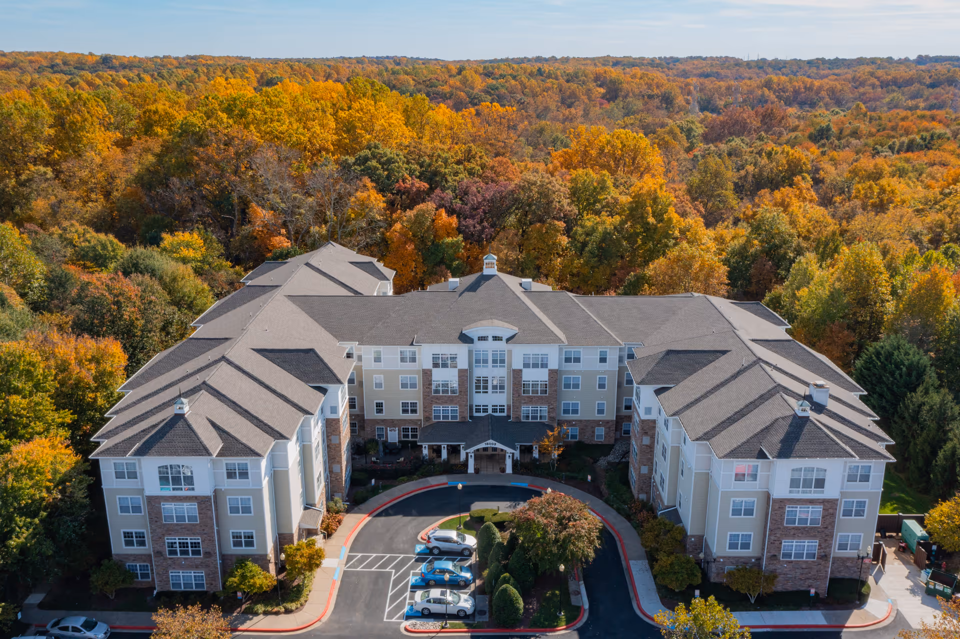 A large, multi-wing senior living building surrounded by autumn trees and a circular driveway.