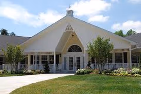 White gabled senior living facility front with porch and landscaped entry.