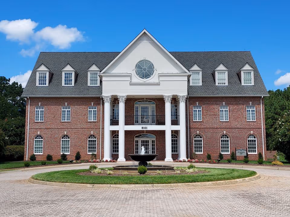 Brick senior living facility with white columns and a circular driveway in front.