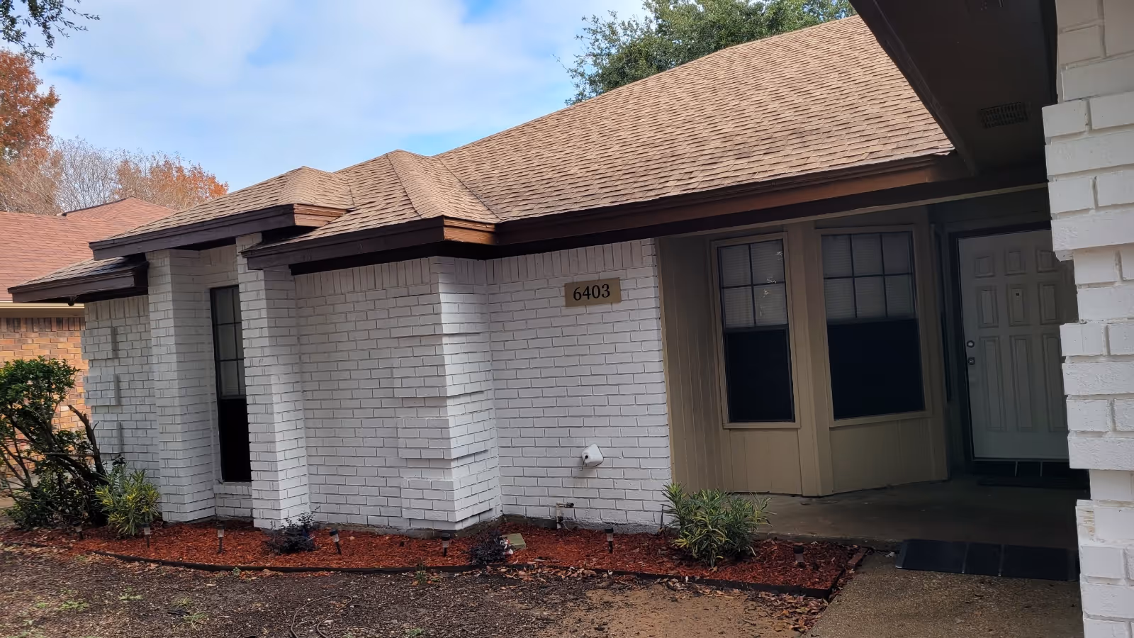 Front exterior of a single-story white brick care home with address number 6403, a covered entryway and small landscaped beds.