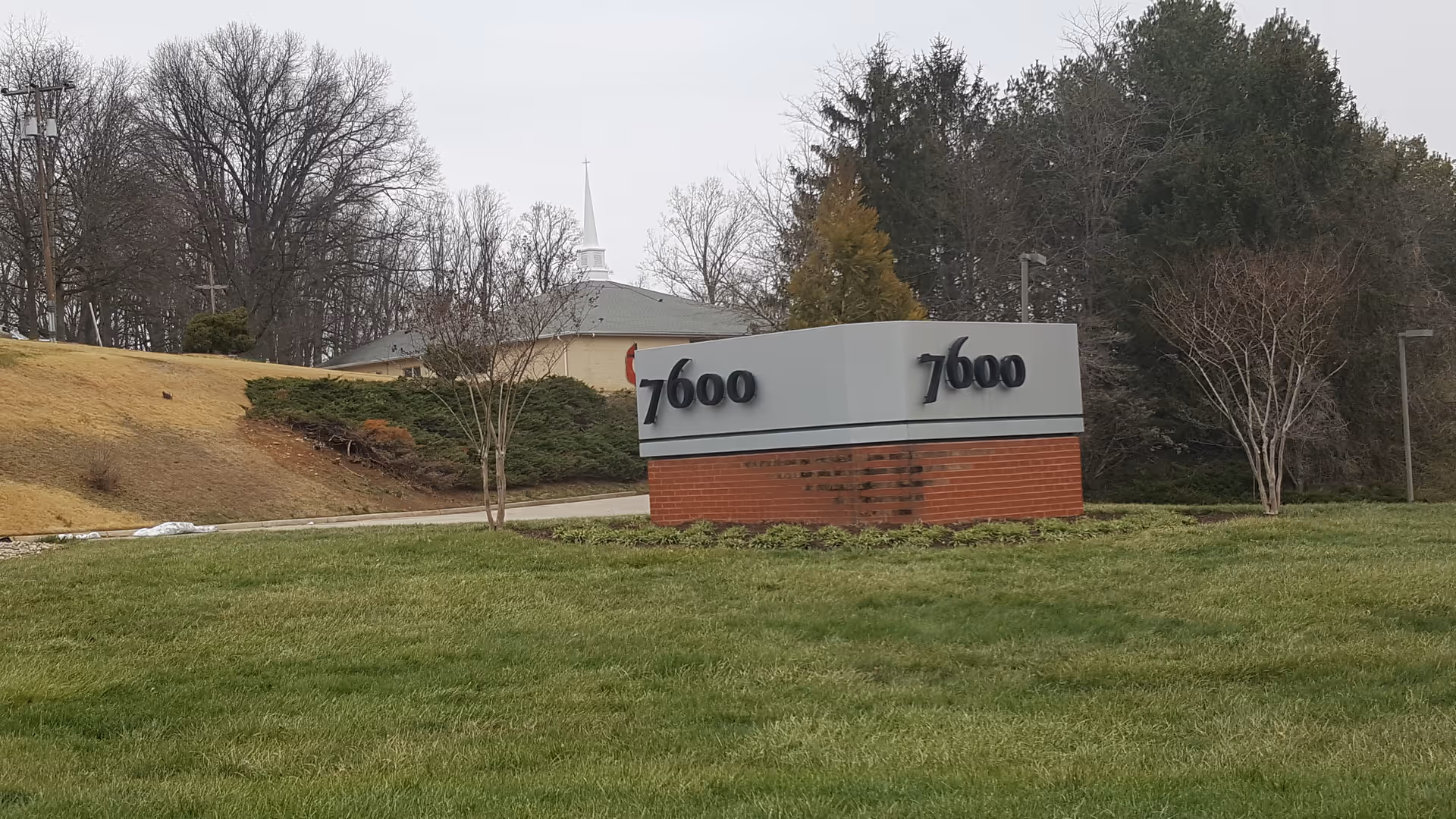 Exterior view of a brick sign with 7600 numbers, lawn, and trees.