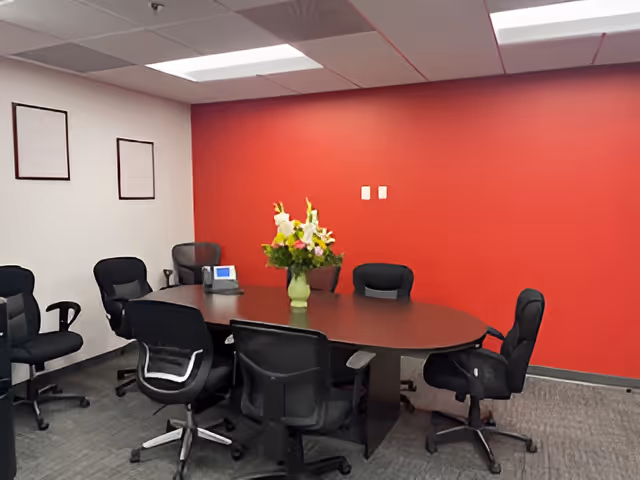 Conference room with oval table, black chairs, red wall, and flower centerpiece.