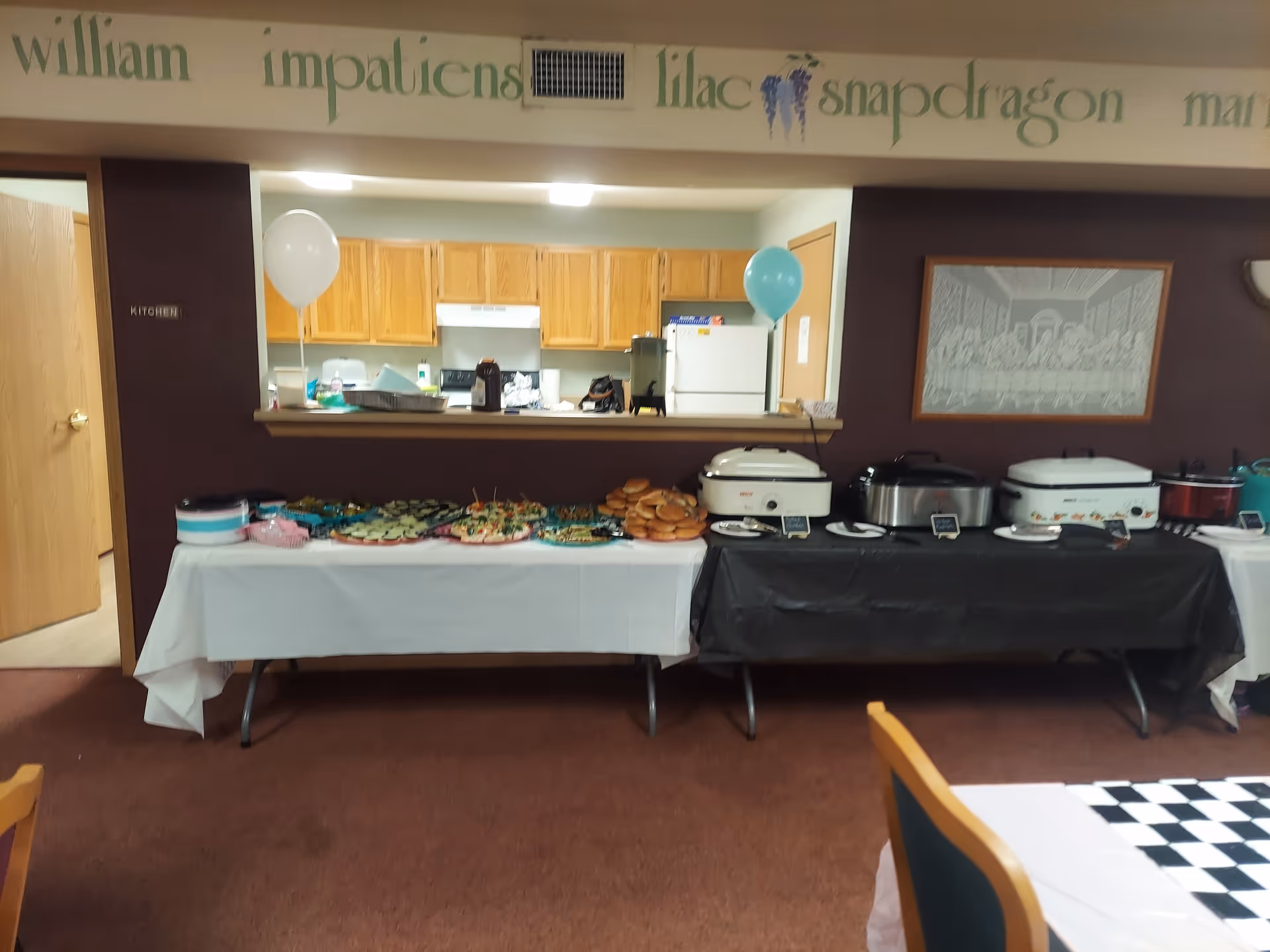Buffet setup with chafing dishes and food trays in a dining area; kitchen visible in back.