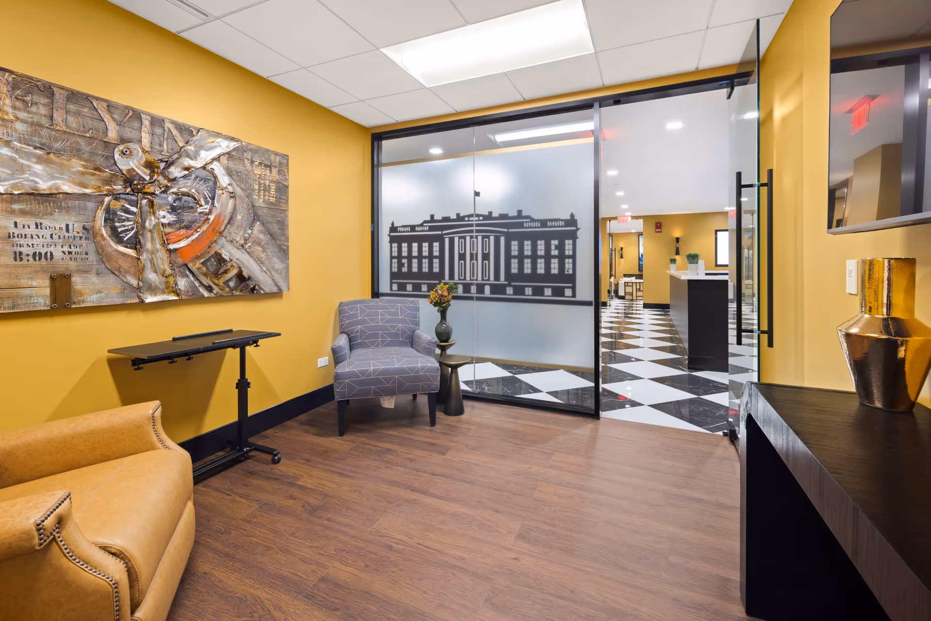Lobby area with yellow walls, wall art, seating, and glass doors leading to a checkered floor.