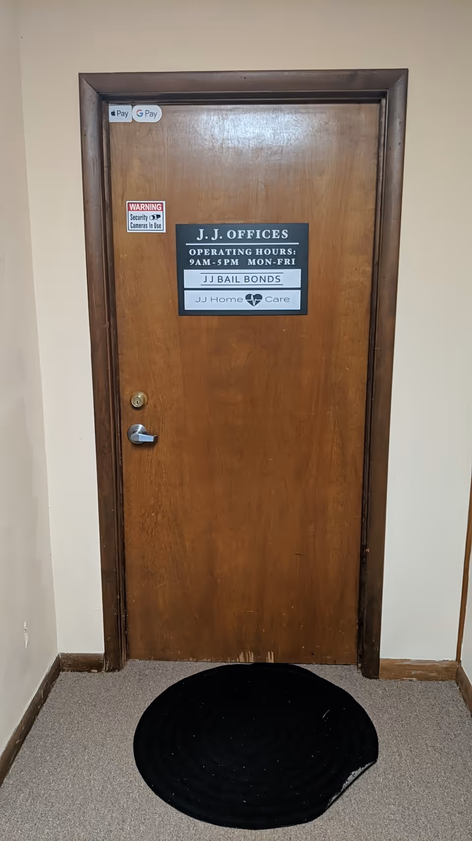 A wooden door labeled J.J. Offices in a hallway with a black circular rug.