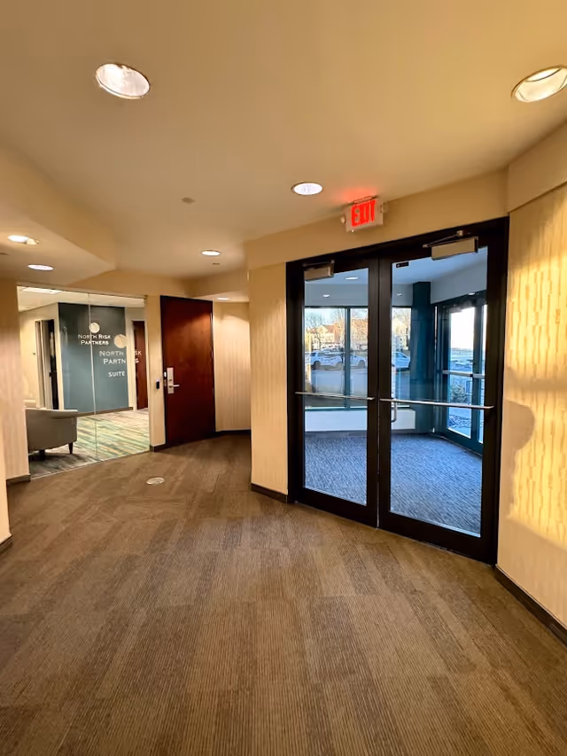 Interior hallway of a senior living facility with glass doors and an exit sign.