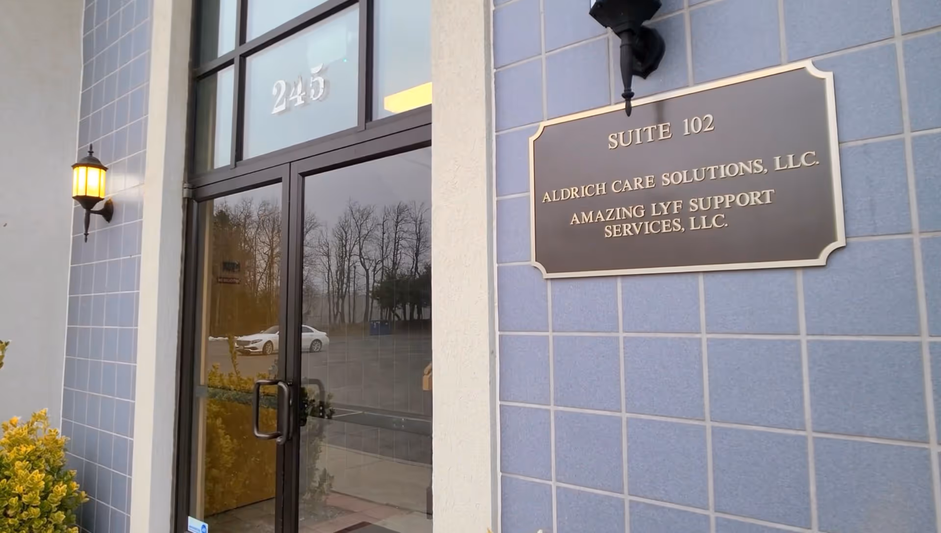 Exterior entrance of Aldrich Care Solutions building with plaque and glass door.