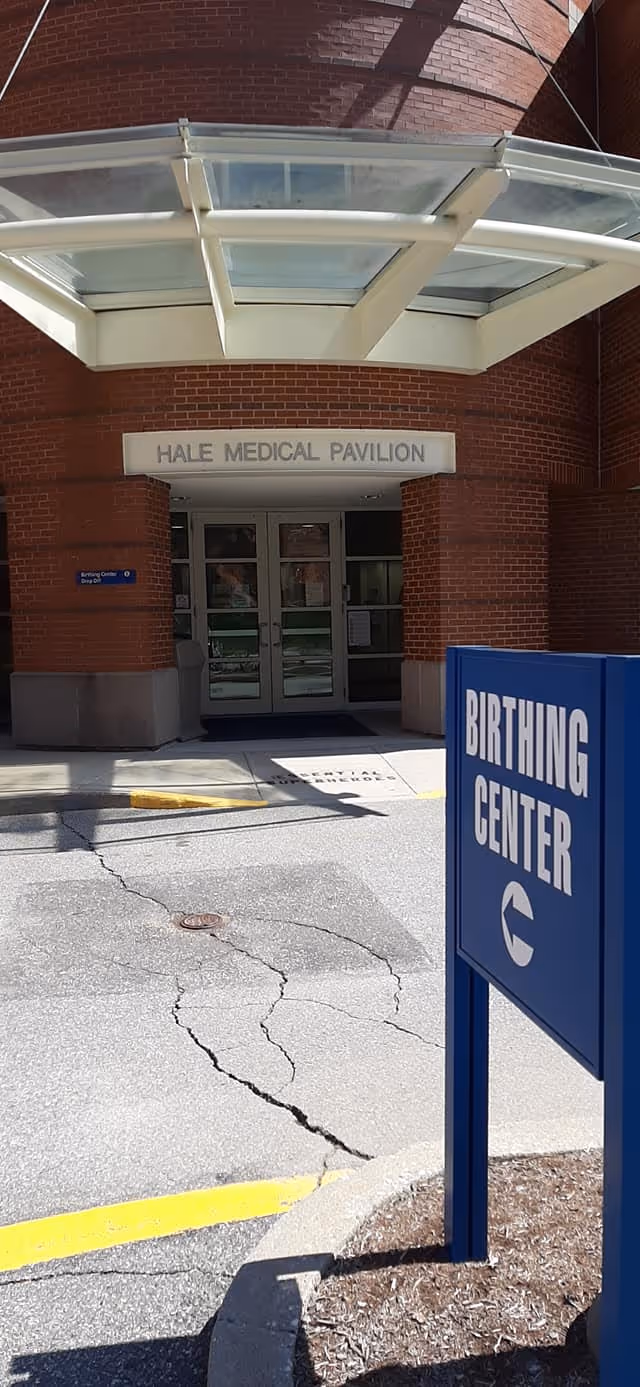 Red brick medical pavilion entrance with glass doors and a blue birthing center sign.