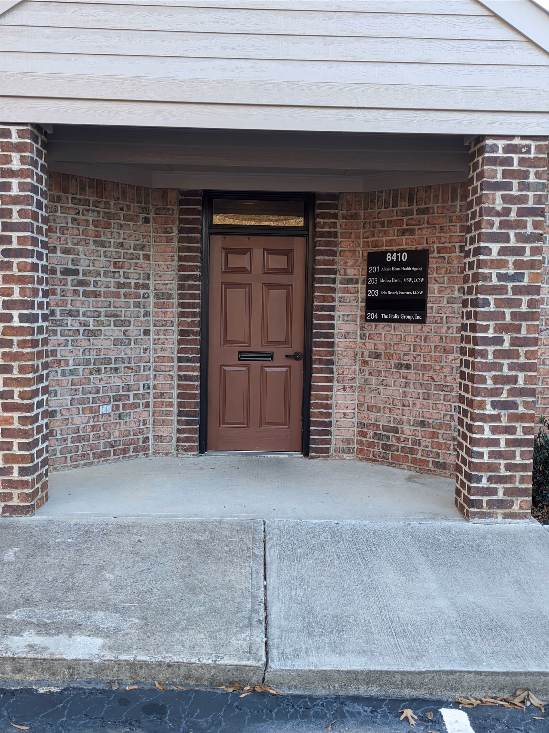 Brick building entrance with brown door and sign plaque listing suite numbers outside.