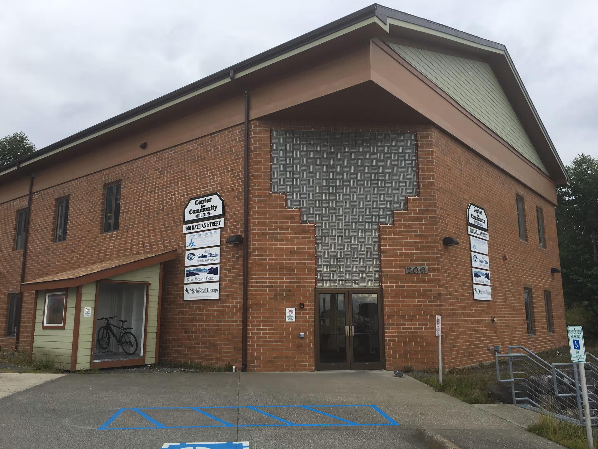 Brick building with large glass block wall, signs, and a front doorway, parking lot in front.