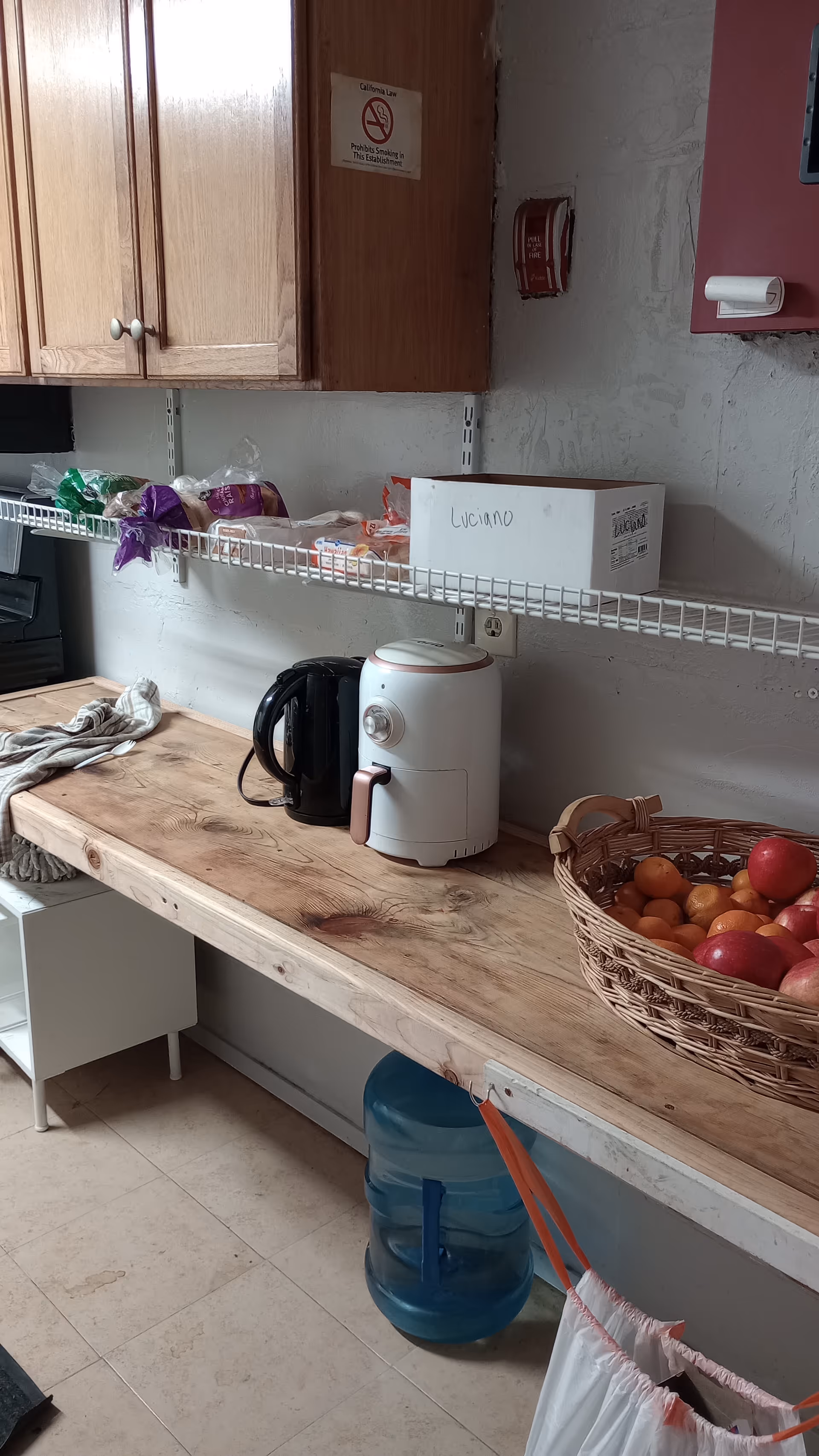 A wooden kitchen counter with appliances, a fruit basket, and a blue water jug.