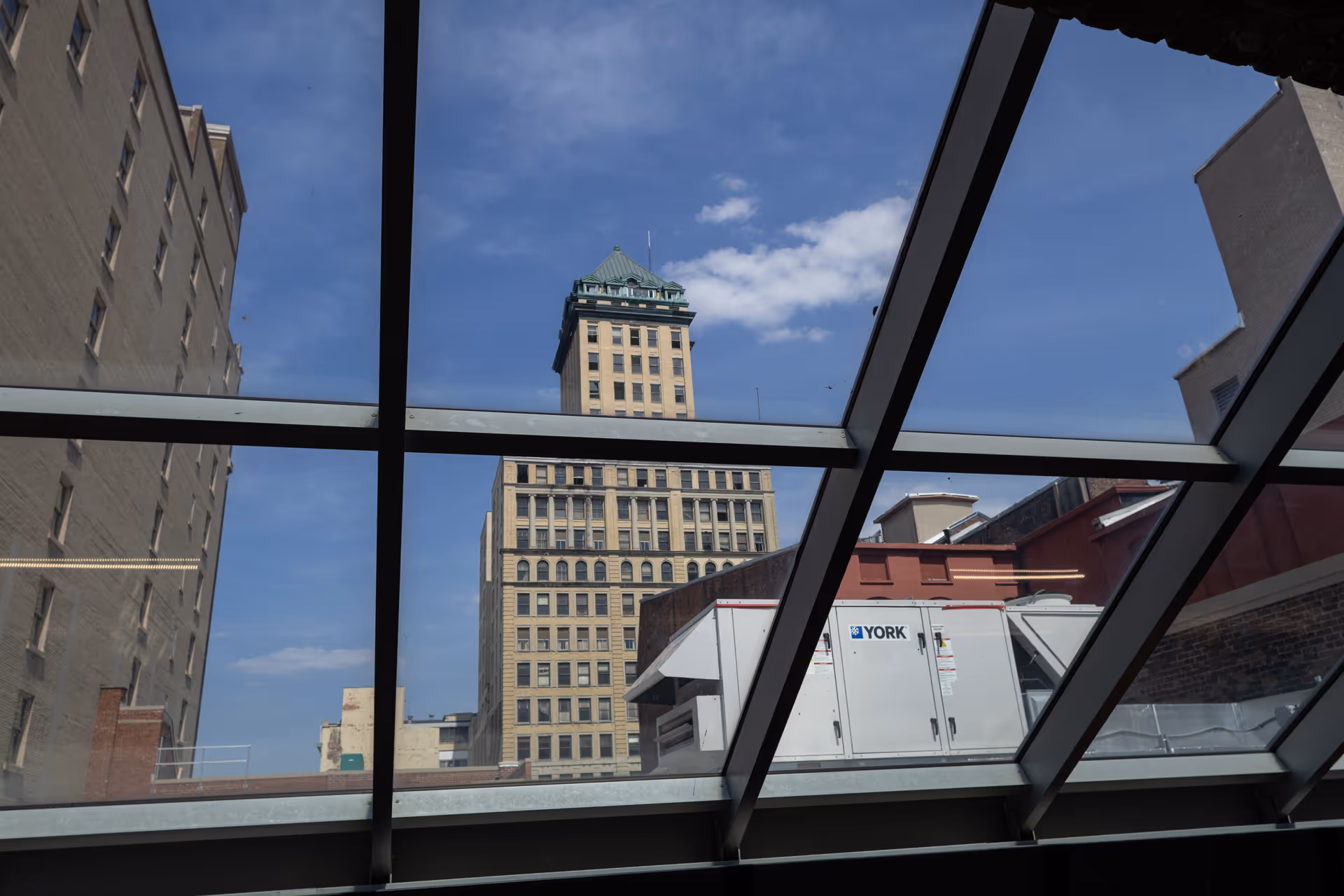 Inside a modern building, a glass skylight frames a city skyline of tall buildings.