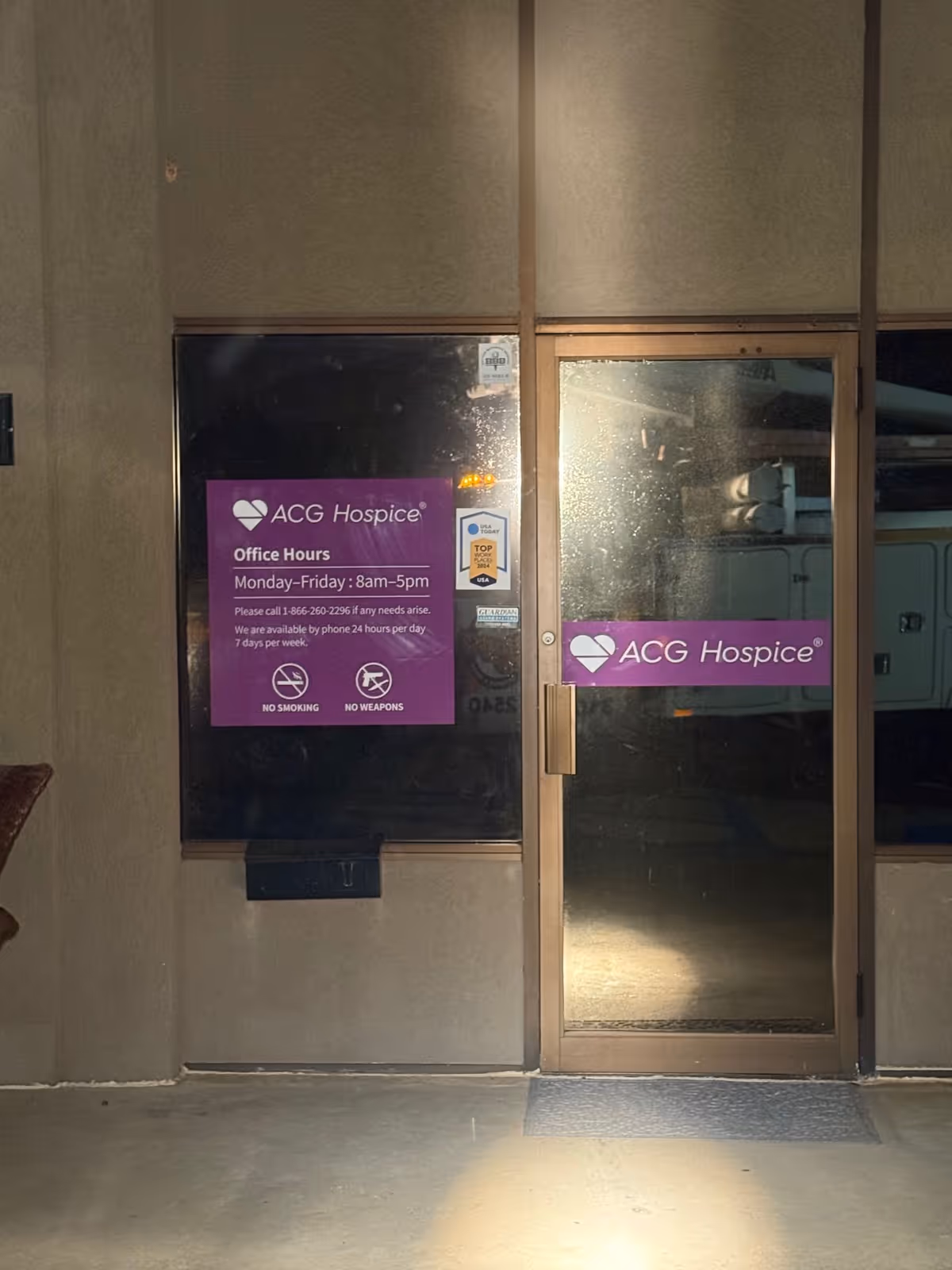 Dimly lit exterior entrance of ACG Hospice with purple signage on glass doors.