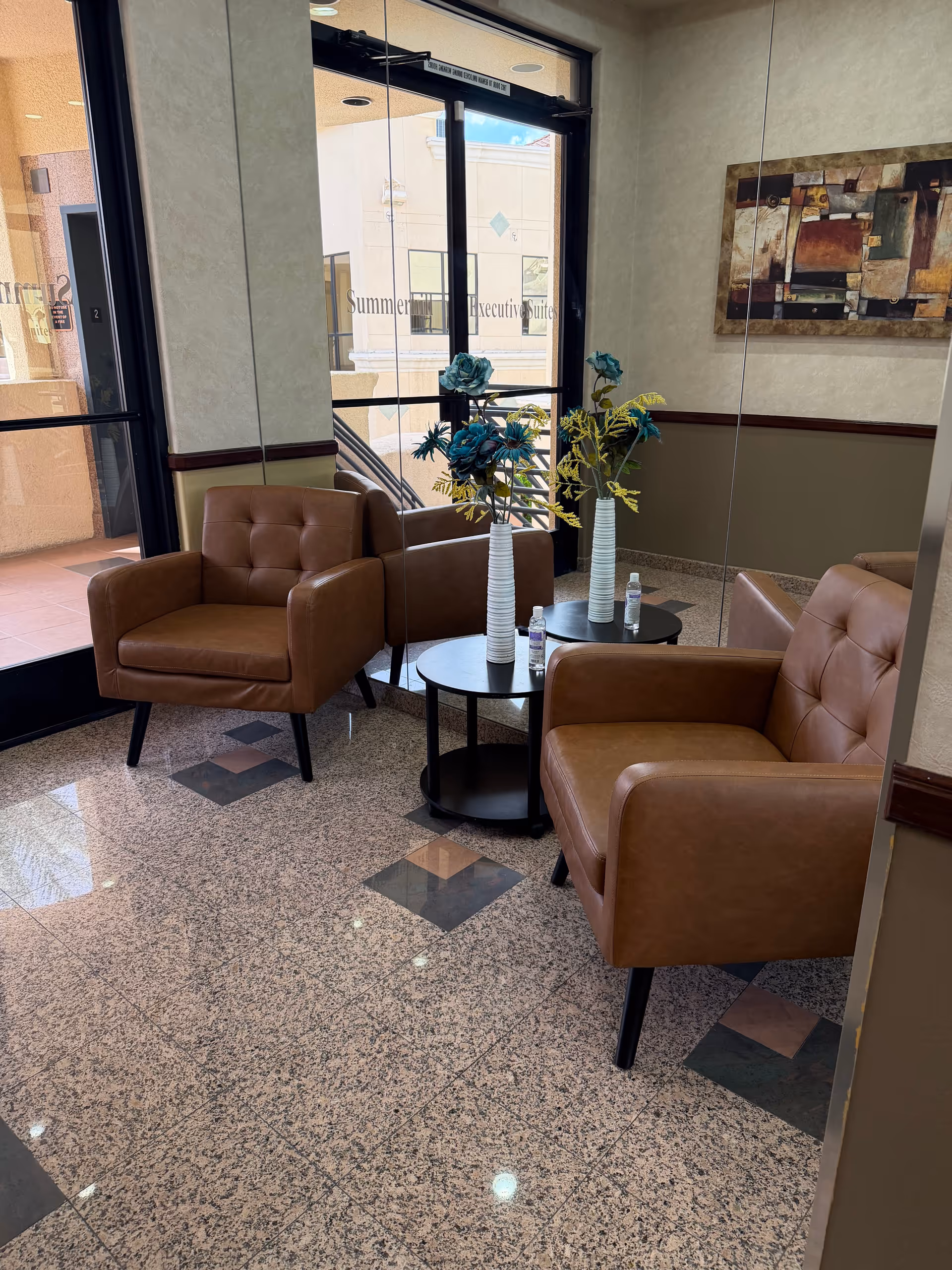 Lobby seating area with brown leather chairs, small tables, and decorative vases.