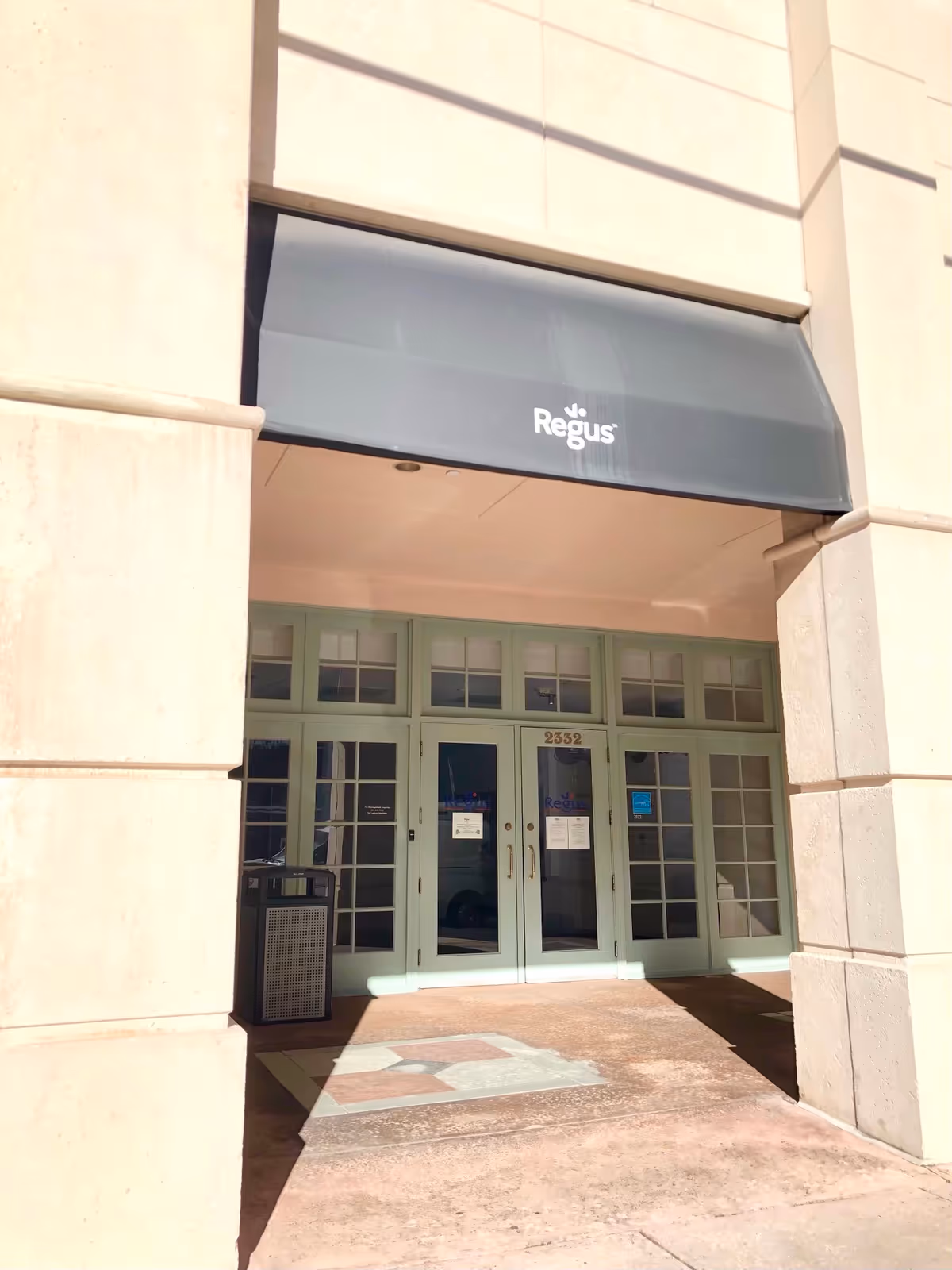 Front entrance of a beige building with Regus awning and glass doors.