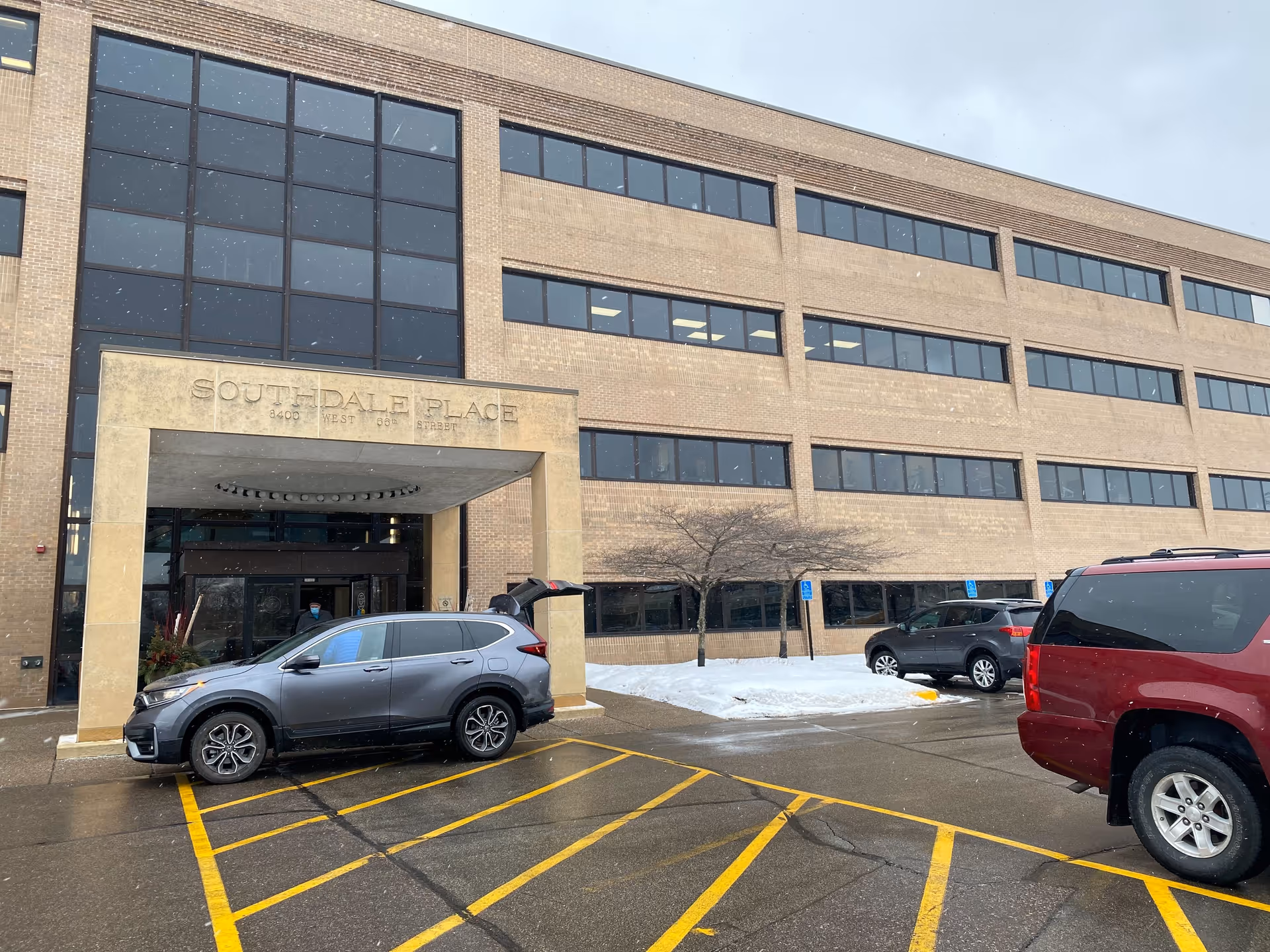Exterior view of a brick building with a covered entrance and parked cars.