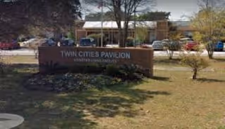 Exterior view of a senior facility with a brick sign and parked cars.