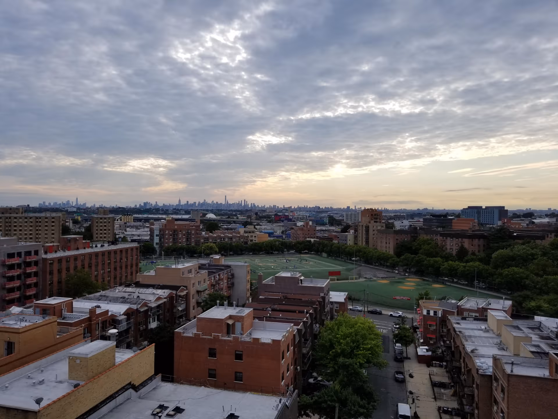 City skyline over a neighborhood with low-rise buildings and a green sports field.