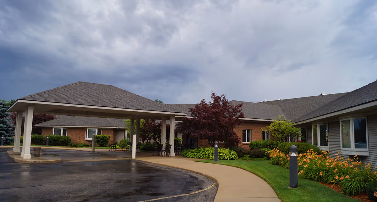 Exterior view of Sheldon Meadows Assisted Living Center with a covered entrance and landscaped walkway.