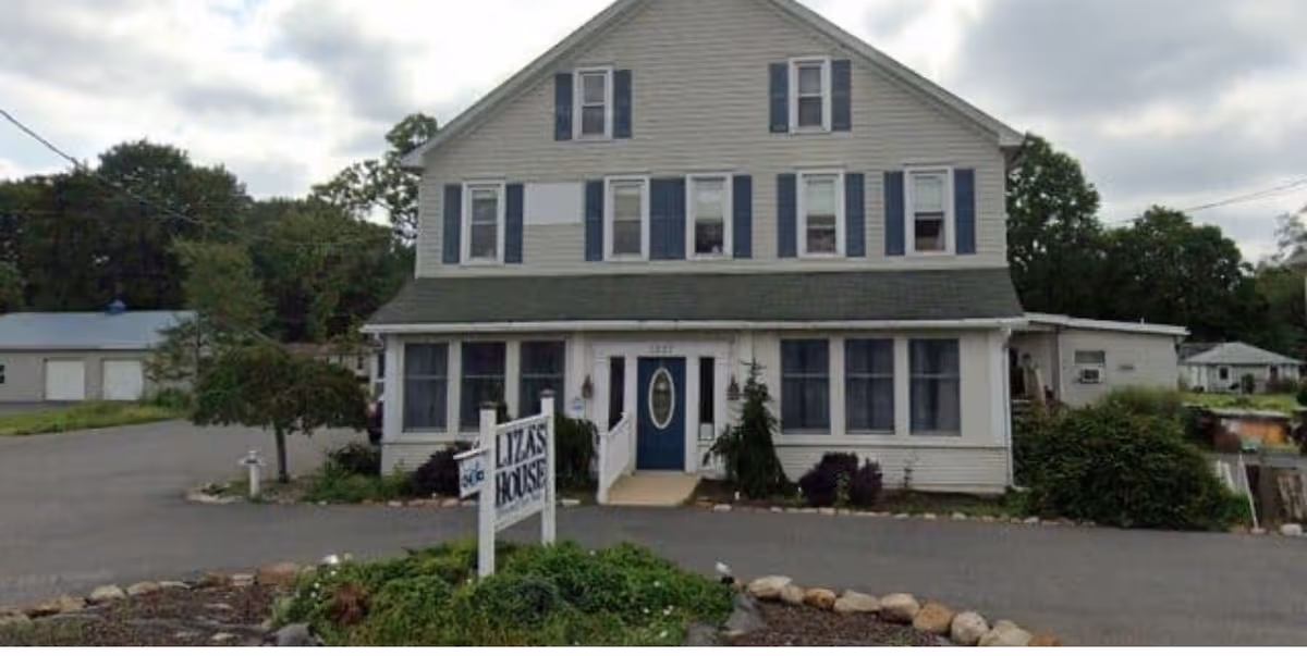 Front view of a white two-story assisted living house with blue shutters and Liza's House sign.
