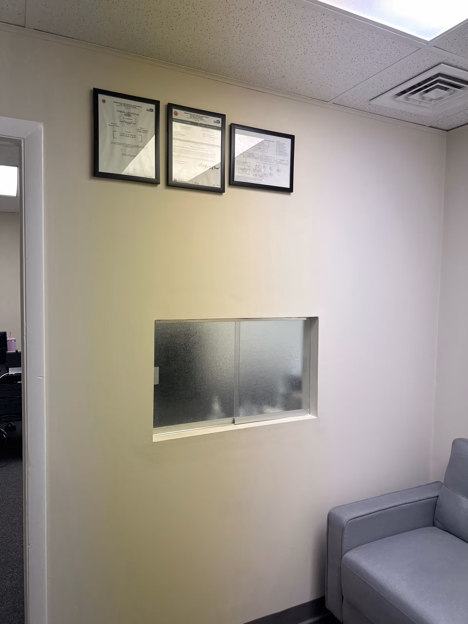 Interior hallway with framed documents, frosted window, doorway, and gray sofa.