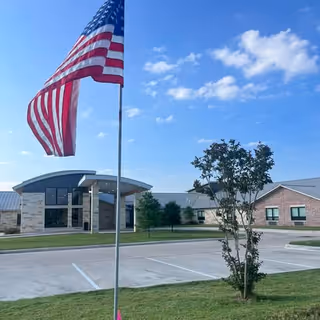 American flag on a pole in front of a brick building entrance with glass doors