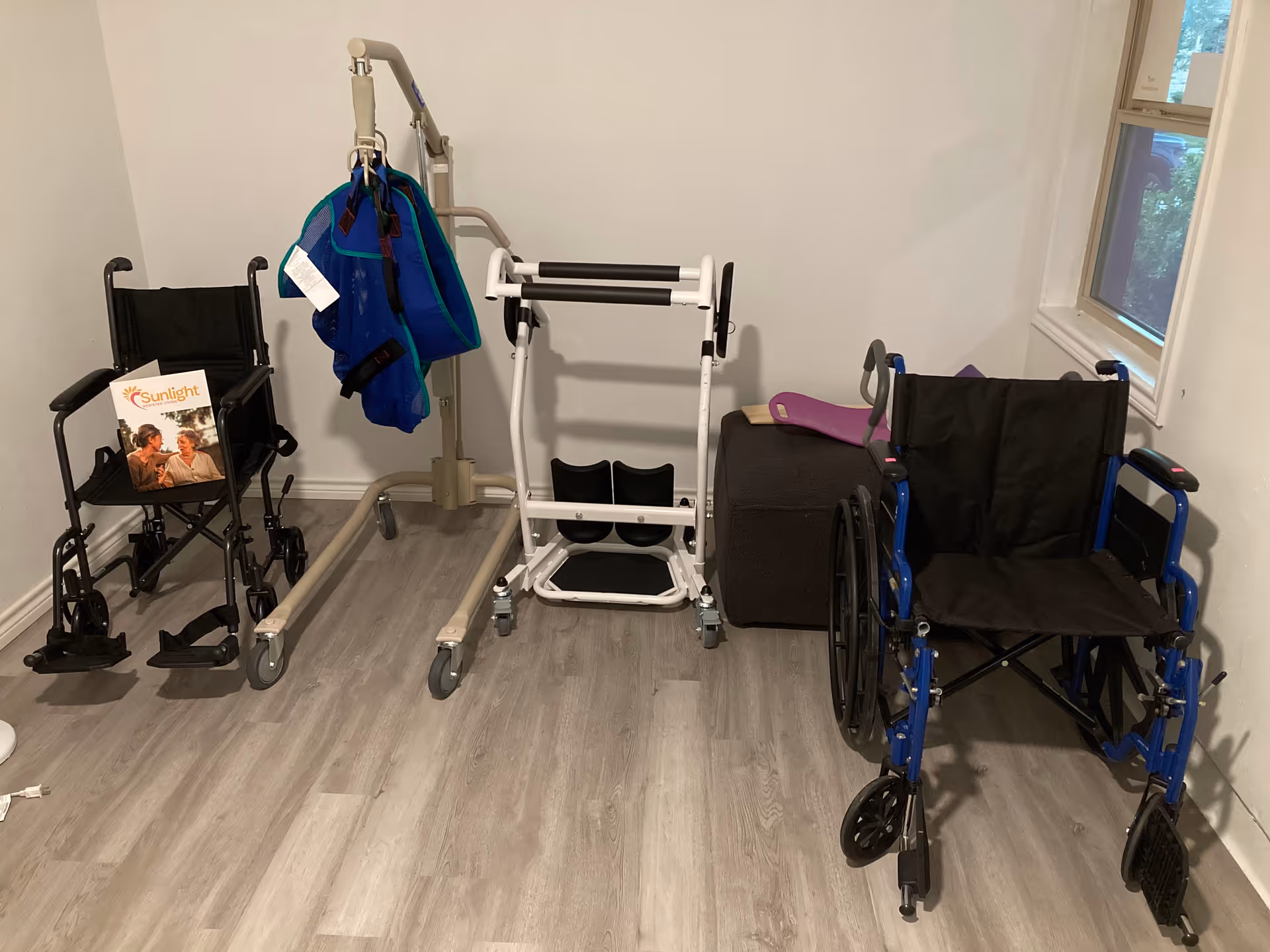 Small room with mobility equipment including wheelchairs and a walker beside a window.