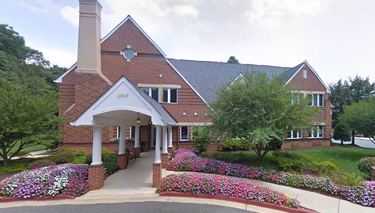 Brick senior living facility exterior with a covered entrance and landscaped flowers.