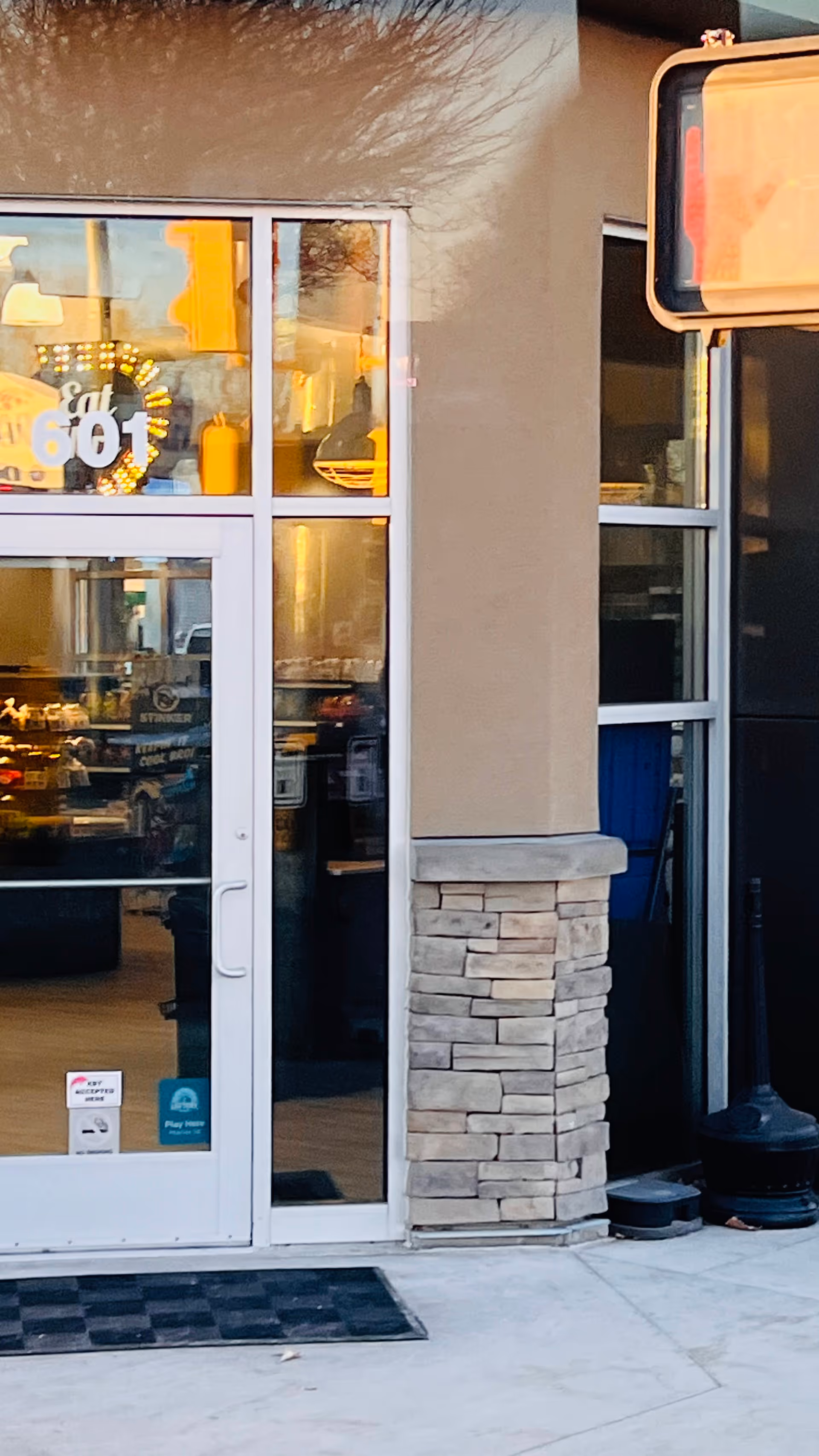 Glass storefront entrance with stone column, beige exterior, interior lights visible through doors and windows.