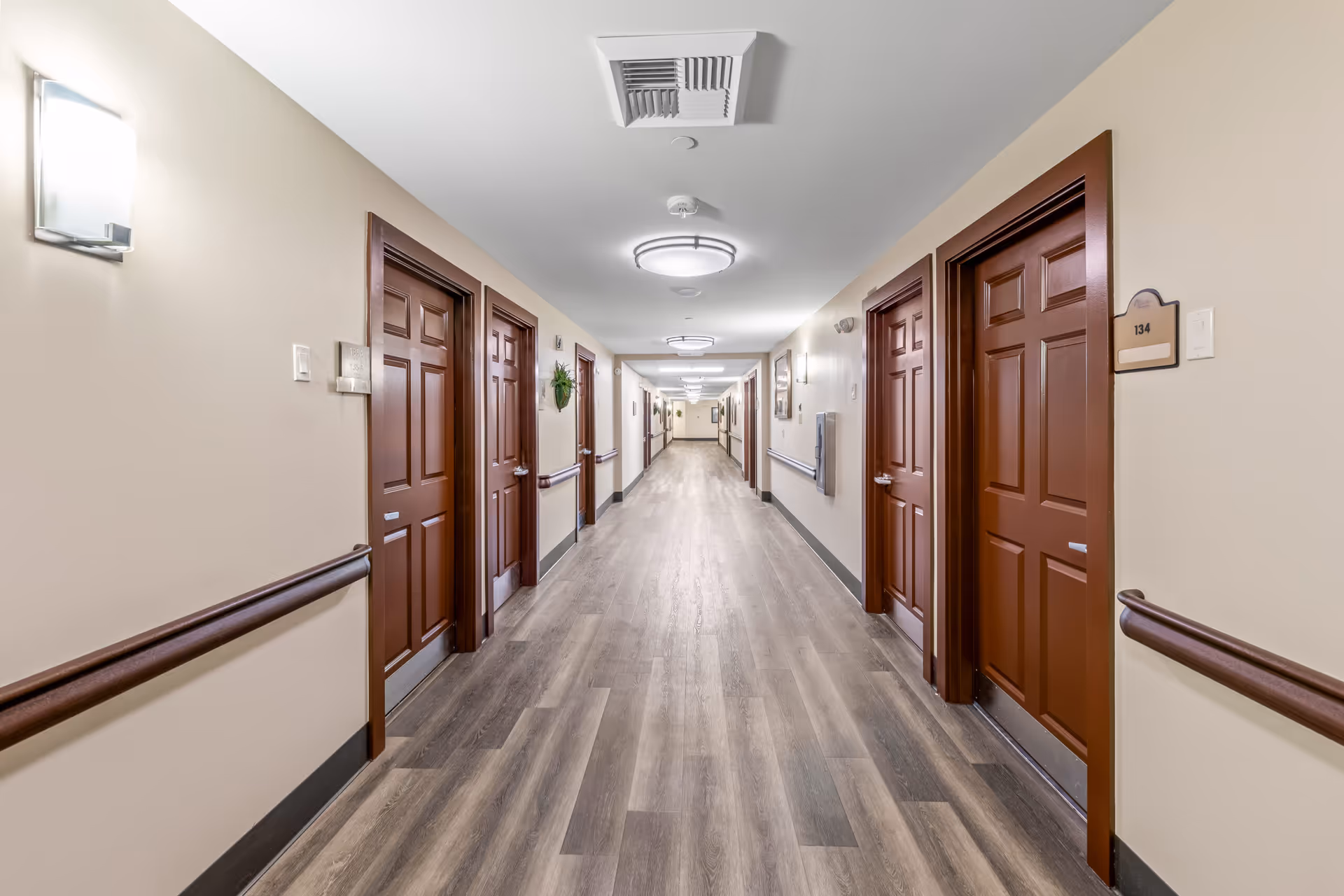 Long corridor with beige walls and wooden doors in a senior living facility.