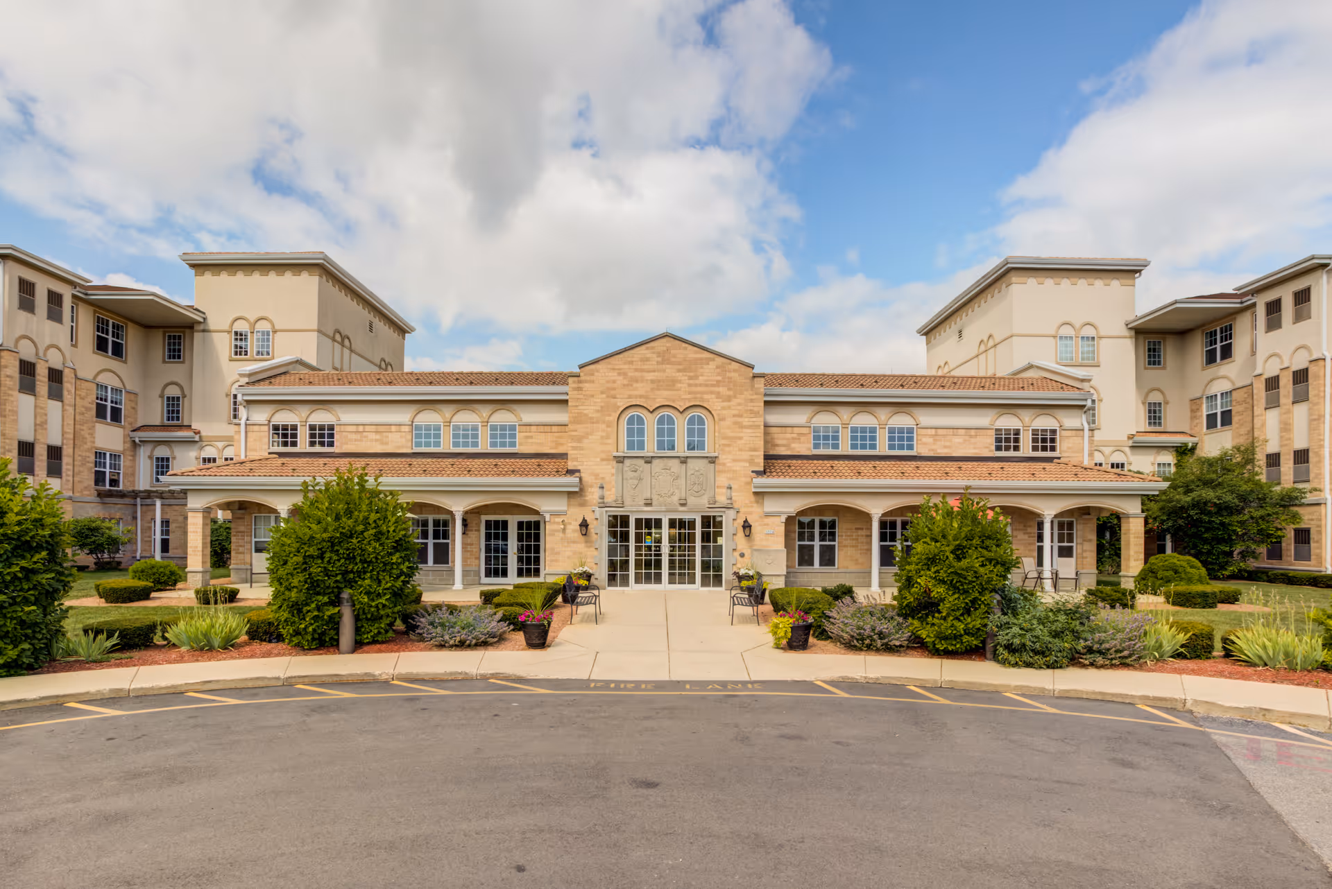 A tan brick, multi-wing senior living facility with a landscaped entrance.
