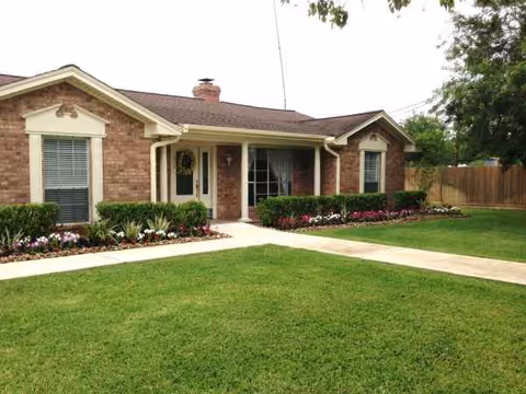 Single-story brick building with a front porch, manicured lawn, and flowerbeds.