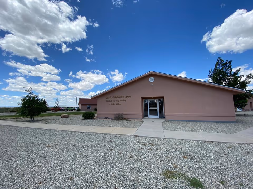 Single-story pink rehabilitation facility building entrance with a gravel front yard and a walkway under a blue sky.