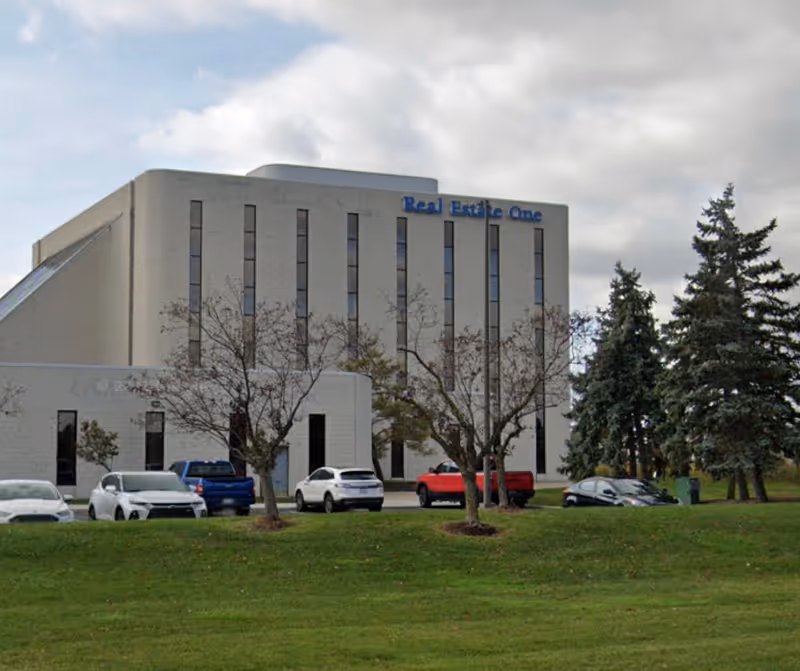 Exterior view of a modern white building with parked cars and trees in front.